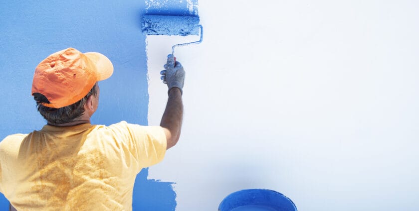 mężczyzna malujący ścianę niebieską farbą